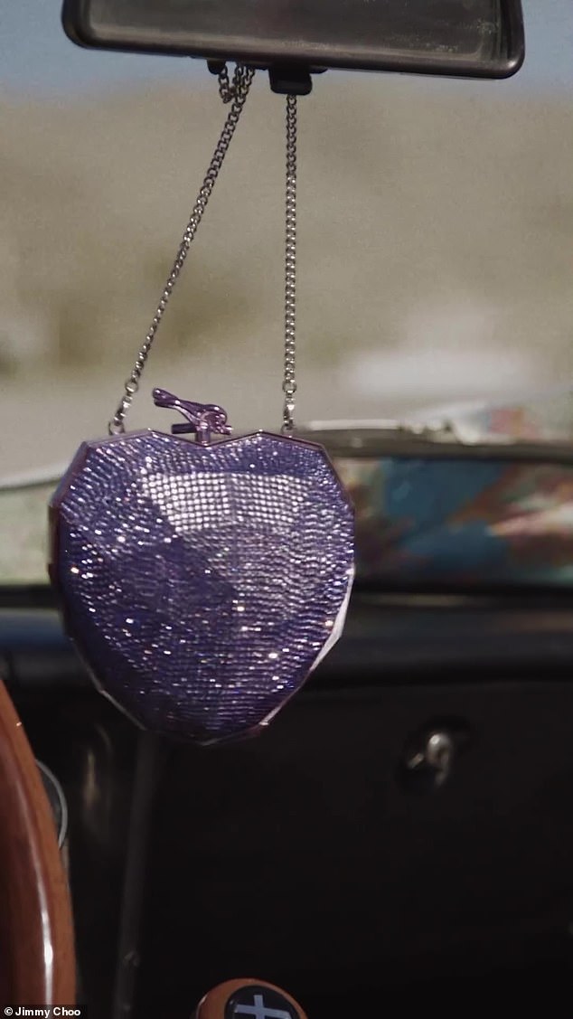 حقيبة يد أرجوانية مبهرة تتدلى من سلاسلها الفضية على مرآة الرؤية الخلفية أثناء القيادة في المدينة