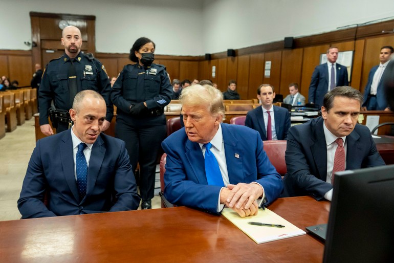 يجلس دونالد ترامب على طاولة الدفاع ويميل نحو محاميه في المحكمة.