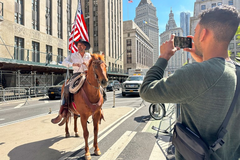 رجل يمتطي حصانًا يحمل العلم الأمريكي خارج محكمة مانهاتن الجنائية.