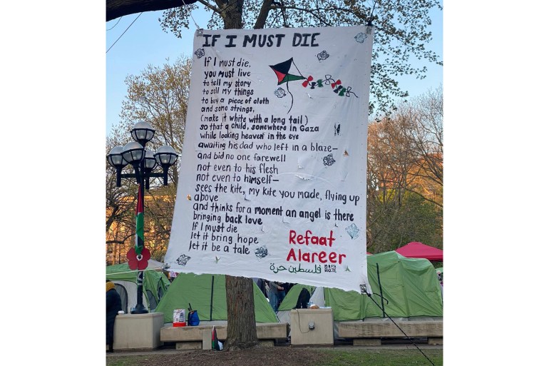 ملصق يحمل نص قصيدة للشاعر الفلسطيني رفعت العرير معلقاً على شجرة في خلفية الخيام